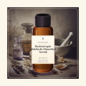 Puede incluir: Una botella de vidrio ámbar con tapa negra y etiqueta blanca que dice HombreOils, Hydratropic Aldehyde Dimethyl Acetal, REF. MO-110, AGE: 24 YEARS, PRODUCED: 2001. Rodeada de frascos de vidrio, un mortero blanco y ramas de lavanda seca.