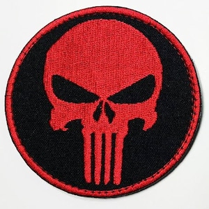 May include: Red and black embroidered patch featuring a skull with a stylized design. The skull is outlined in black and has a red fill. The patch is circular and has a black border.