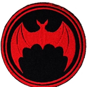 Puede incluir: Parche bordado circular con un diseño de murciélago rojo sobre fondo negro, enmarcado por un borde rojo y negro. El murciélago tiene alas detalladas. Ideal para personalizar ropa o accesorios.