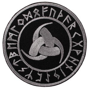 May include: Round black patch with a silver-gray triple-horn design in the center, surrounded by a silver-gray border with runic lettering. The patch is likely for clothing or accessories.