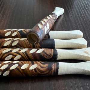 May include: A collection of wooden smoking pipes. The pipes have a dark brown, patterned body with white leaf-shaped cutouts. The mouthpiece is a light-colored wood. The pipes are arranged on a dark brown surface.