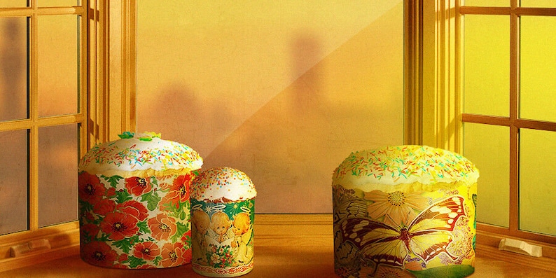 Może przedstawiać: Trzy ozdobne ciasta wielkanocne, jedno z motywem motyla, jedno z motywem kwiatowym, a jedno z motywem dziecięcym. Ciasta stoją na drewnianej powierzchni przed oknem.