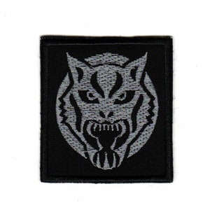 Op de afbeelding: Een zwarte geborduurde patch met een zilvergrijs tijgerkopontwerp. De bek van de tijger is open en zijn tanden zijn zichtbaar.