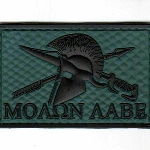 May include: A rectangular patch with a dark green background and a black border. The patch features a black Spartan helmet, crossed spears, and a sword. The Greek phrase "MOLON LABE" is displayed in black letters.