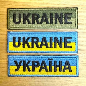 Peut inclure: Trois écussons brodés avec le mot "UKRAINE". Le patch supérieur est vert olive. Le patch du milieu est bleu et jaune. Le patch inférieur est bleu et jaune avec le mot "YKPAlHA" en caractères cyrilliques.