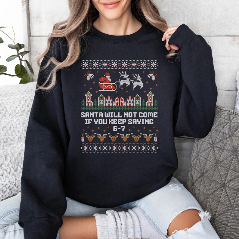 May include: Black sweatshirt with a festive Christmas design. The design includes Santa in a sleigh, reindeer, houses, and the text "SANTA WILL NOT COME IF YOU KEEP SAYING 6-7". The design is in red, white, and green.