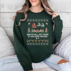 May include: Dark green Christmas sweatshirt with a festive design. The design includes Santa in a sleigh, reindeer, houses, and the text "SANTA WILL NOT COME IF YOU KEEP SAYING 6-7."