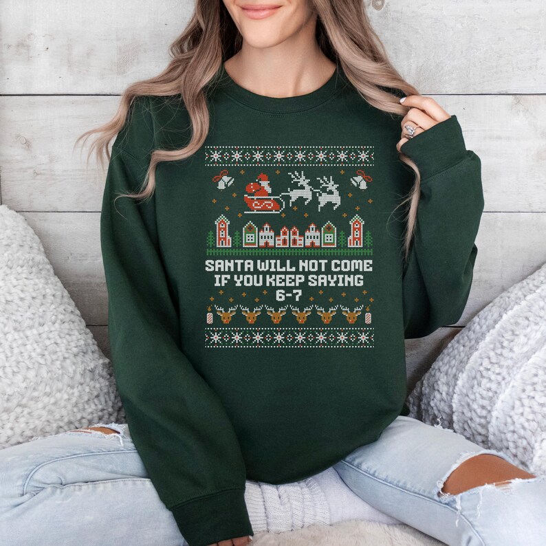 May include: Dark green Christmas sweatshirt with a festive design. The design includes Santa in a sleigh, reindeer, houses, and the text "SANTA WILL NOT COME IF YOU KEEP SAYING 6-7."