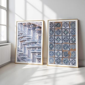 May include: Two framed art prints with gold frames. One print shows ornate, blue and white architectural columns. The other displays a pattern of blue and white tiles with geometric designs. Both are leaning against a white wall.