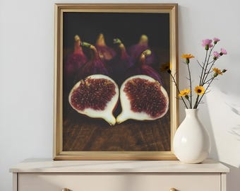 May include: A framed print featuring a close-up of two fig halves, revealing the fruit's red interior and white flesh. The background shows whole figs and a dark surface. A white vase with flowers sits to the right.