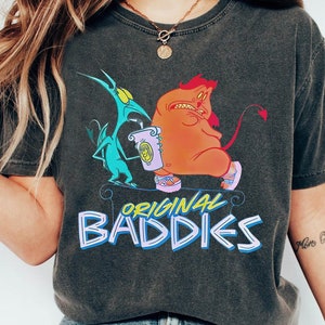 May include: A black t-shirt featuring a graphic print of two cartoon characters, one green and one orange, with the text "ORIGINAL BADDIES" underneath. The characters are holding a cup of coffee.