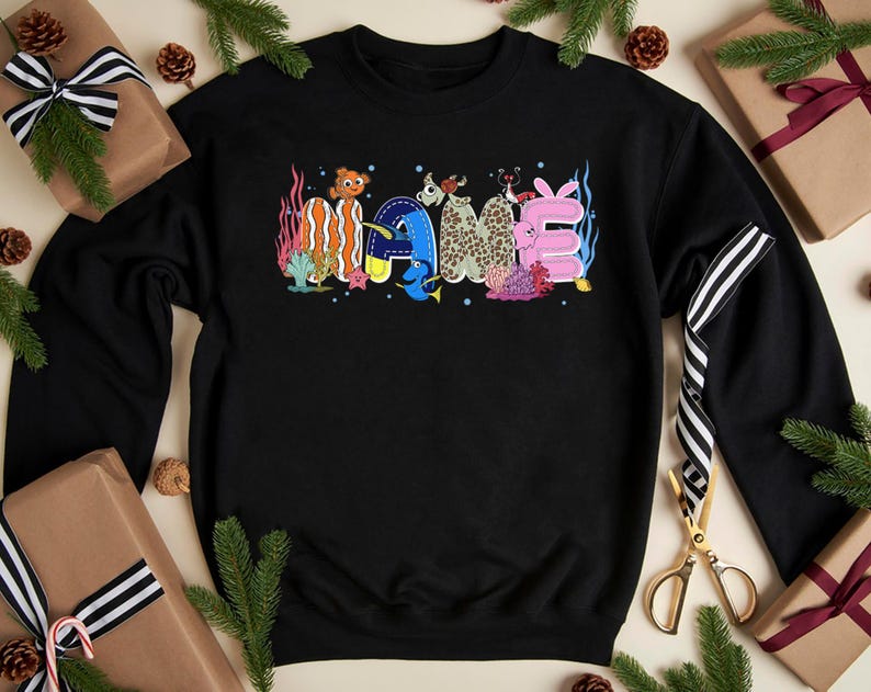 May include: Black sweatshirt with the word "NAME" in colorful, whimsical lettering. The letters are decorated with sea creatures and coral, creating a playful, underwater theme. A fun, casual top.