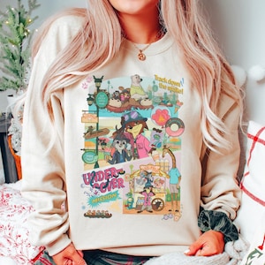 May include: Beige sweatshirt with a colorful cartoon graphic. The graphic features various animal characters in a park setting, with text that reads "Track down the snake!" and "Undercover Mission."