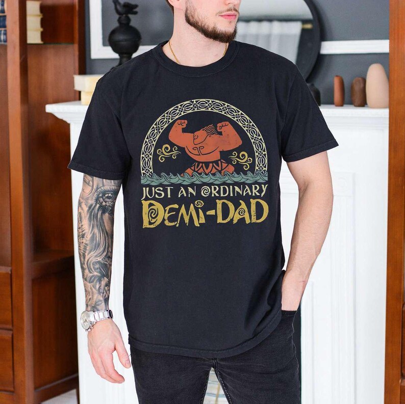 Op de afbeelding: Zwart T-shirt met een vintage-stijl grafische afbeelding van een gespierd cartoonfiguur met de tekst "Just an ordinary Demi-Dad".