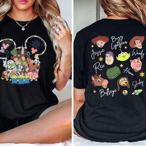 Pu&ograve; includere: T-shirt nera con un design a tema Disney. La parte anteriore mostra un contorno della testa di Topolino con fuochi d'artificio e personaggi di Toy Story. Il retro presenta volti di personaggi e nomi come Buzz Lightyear e Woody.