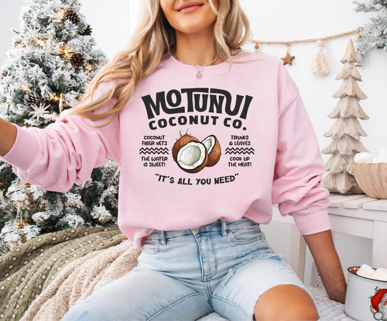 May include: A light pink sweatshirt with the text "MOTUNUI COCONUT CO." and a graphic of a coconut. The sweatshirt also features text about coconut fiber nets, trunks & leaves, and the phrase "IT'S ALL YOU NEED".