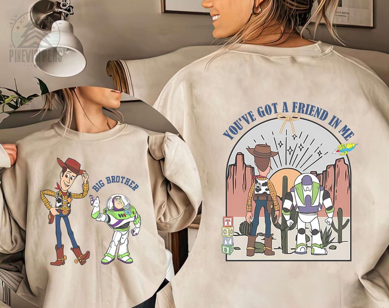 May include: Beige sweatshirt featuring cartoon characters Woody and Buzz Lightyear from Toy Story. The front displays Woody and Buzz with the text "Big Brother." The back has a desert scene with the text "You've Got a Friend in Me."