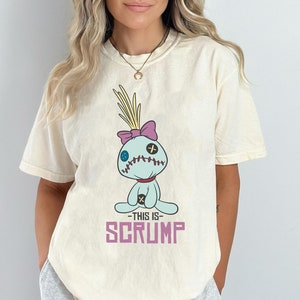 May include: A white t-shirt with a cartoon image of a blue and purple Stitch doll with the text "This is Scrump" printed on the front.