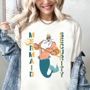 May include: White t-shirt with a graphic of a cartoon King Triton holding a trident and the words "Mermaid Security" printed vertically on either side of him.
