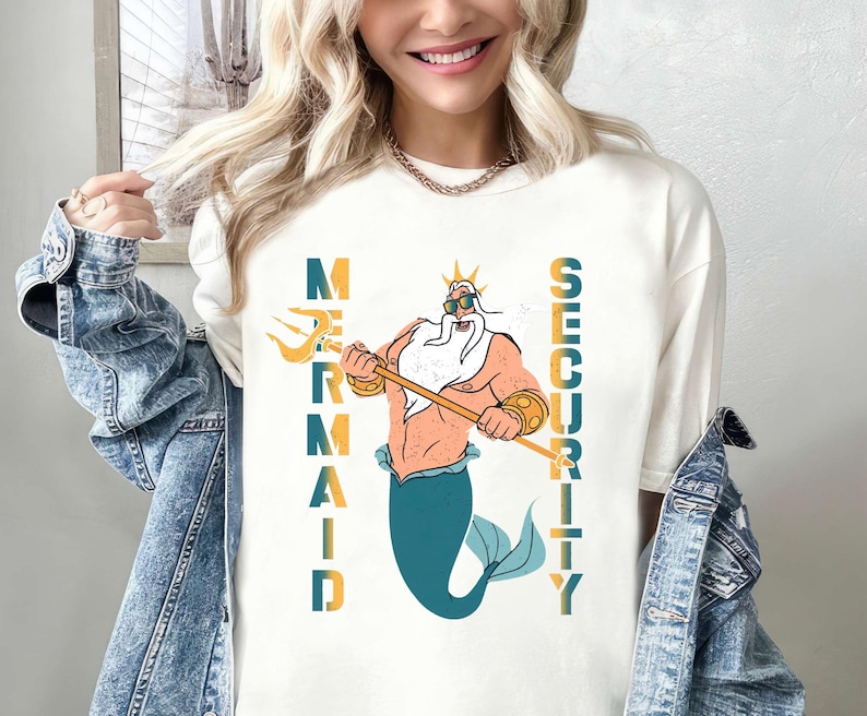 May include: White t-shirt with a graphic of a cartoon King Triton holding a trident and the words "Mermaid Security" printed vertically on either side of him.
