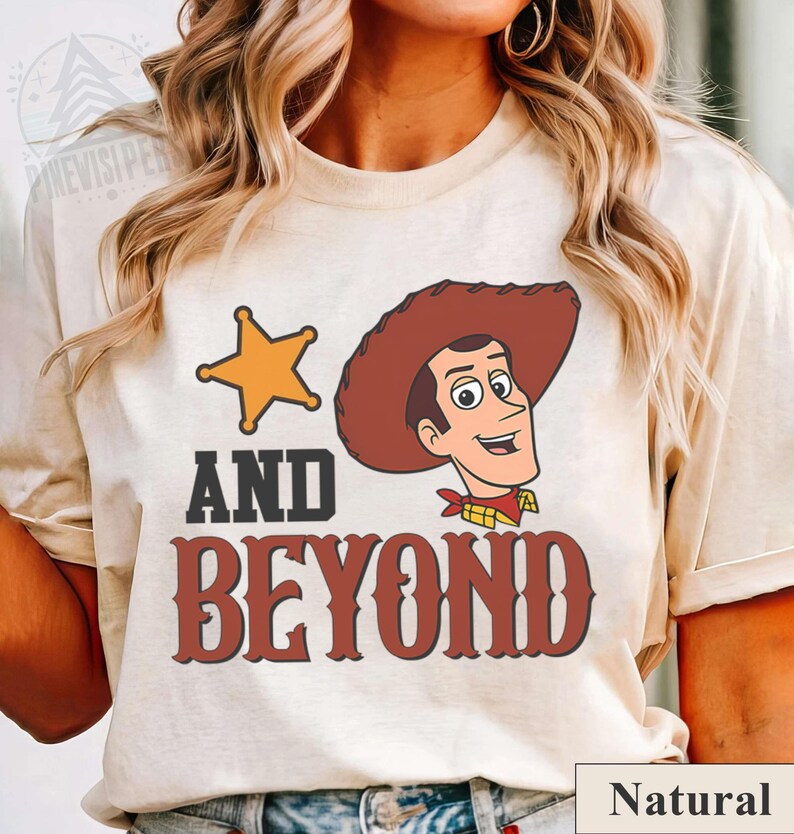 May include: A natural-colored t-shirt featuring a cartoon image of a cowboy with a sheriff's star and the words "AND BEYOND" in a western-style font. The shirt has a crew neck and short sleeves.
