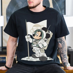 May include: Black t-shirt with a graphic of Mickey Mouse dressed as an astronaut holding a flag that says "Space Mountain".