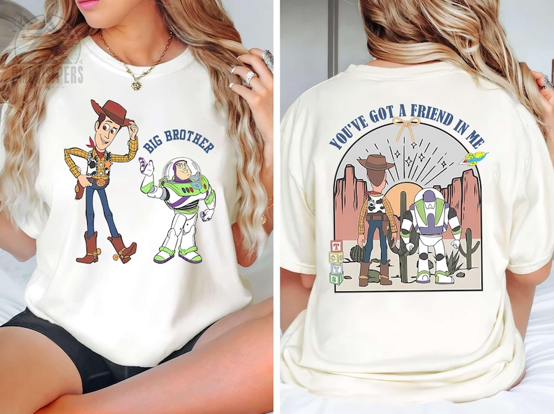 May include: Cream-colored t-shirt featuring cartoon characters Woody and Buzz Lightyear. The front of the shirt has the text "BIG BROTHER". The back of the shirt has the text "YOU'VE GOT A FRIEND IN ME".