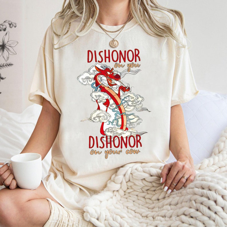 Puede incluir: Una camiseta de color crema con un gr&aacute;fico de drag&oacute;n rojo y el texto "Dishonor on you, Dishonor on your cow."