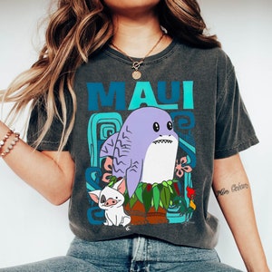 Puede incluir: Una camiseta gris oscuro con un estampado gr&aacute;fico colorido de un tibur&oacute;n, un cerdo y un gallo de dibujos animados. El texto "MAUI" est&aacute; impreso en azul y verde en la camiseta.