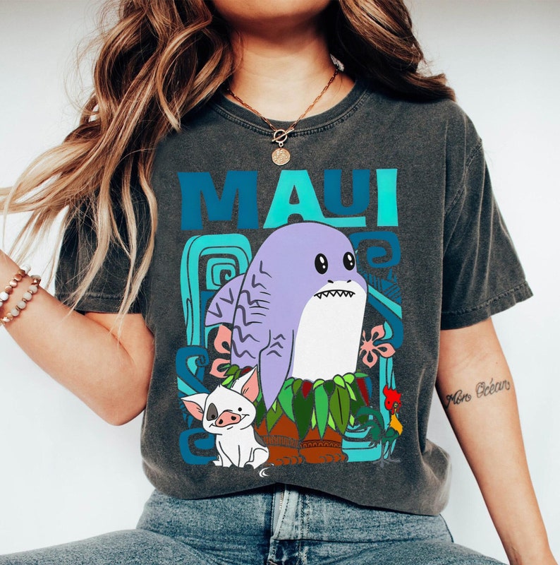Puede incluir: Una camiseta gris oscuro con un estampado gr&aacute;fico colorido de un tibur&oacute;n, un cerdo y un gallo de dibujos animados. El texto "MAUI" est&aacute; impreso en azul y verde en la camiseta.