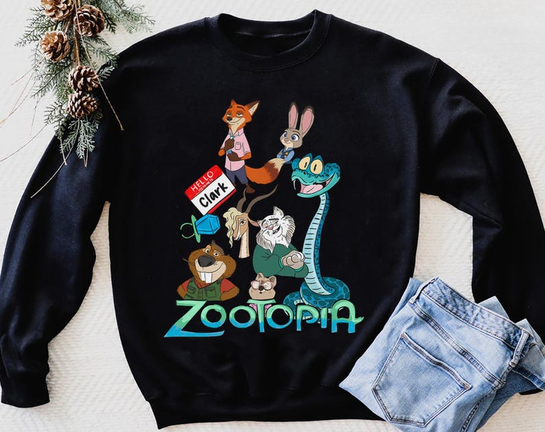 Puede incluir: Sudadera negra con un dise&ntilde;o colorido con personajes de la pel&iacute;cula animada Zootopia. El dise&ntilde;o incluye un zorro, un conejo y una serpiente. La palabra "Zootopia" est&aacute; escrita en azul y verde. Una etiqueta con el nombre dice "Hello Clark".