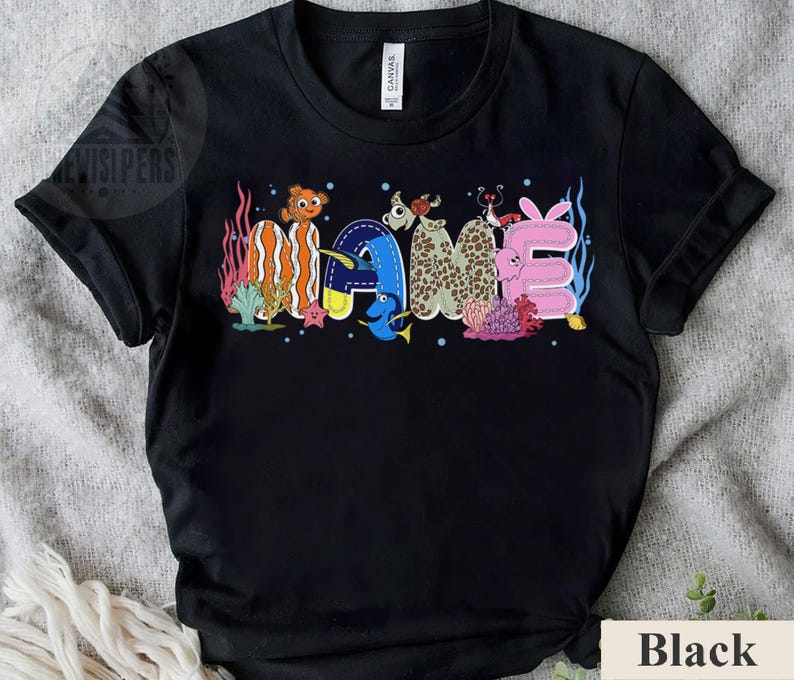 May include: Black t-shirt with the word "GAME" in colorful, cartoon-style lettering. The letters are designed with aquatic themes, including fish and coral, creating a playful and vibrant design. The shirt is made of a soft material.