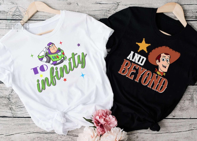 May include: Two t-shirts, one white and one black, with cartoon graphics. The white shirt features Buzz Lightyear with the text "To Infinity" in green and purple. The black shirt displays Woody with the text "And Beyond" in brown.