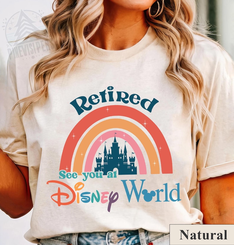 K&ouml;nnte beinhalten: Ein wei&szlig;es T-Shirt mit einem Regenbogen-Design und dem Text "Retired See you at Disney World". Der Regenbogen hat eine Silhouette von Schloss Aschenputtel in der Mitte. Der Text ist in blauer, lila und rosa Schrift. Das Shirt ist mit "Natur" gekennzeichnet.