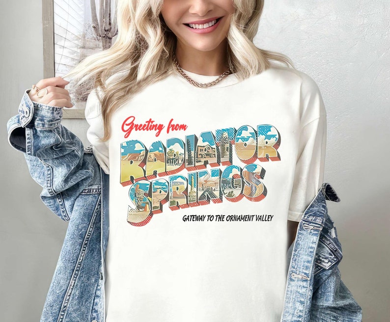 K&ouml;nnte beinhalten: Wei&szlig;es T-Shirt mit einer Grafik im Stil einer Vintage-Postkarte mit der Aufschrift "Greeting from Radiator Springs, Gateway to the Ornament Valley".