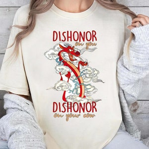 Puede incluir: Una camiseta de color crema con una ilustraci&oacute;n de un drag&oacute;n rojo y el texto "Dishonor on you, Dishonor on your cow."