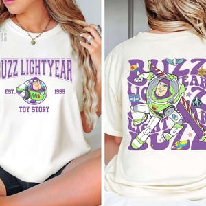 May include: Cream-colored t-shirt featuring Buzz Lightyear from Toy Story. The front displays "Buzz Lightyear" in purple arched text, with the character's image and "Est. 1995, Toy Story." The back shows Buzz in action with the same text.