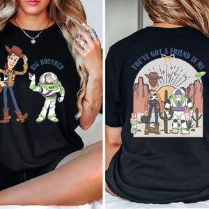 May include: Black t-shirt featuring Woody and Buzz Lightyear from Toy Story. The front of the shirt says "Big Brother" above the characters. The back of the shirt says "You've got a friend in me" with the characters and a desert scene.