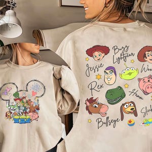 Pu&ograve; includere: Felpa beige con un design a testa di Topolino con personaggi di Toy Story. Il retro mostra i volti e i nomi dei personaggi, tra cui Buzz Lightyear, Woody e Jessie. Un design divertente e colorato.