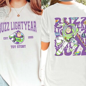 May include: White t-shirt featuring a Buzz Lightyear graphic from Toy Story. The front displays "Buzz Lightyear" in purple, with an image of Buzz and the text "Toy Story 1995". The back shows Buzz in action with the words "Buzz Lightyear".