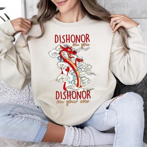 Puede incluir: Una sudadera de color crema con una ilustraci&oacute;n de un drag&oacute;n rojo y el texto "Dishonor on you Dishonor on your cow" impreso en ella.