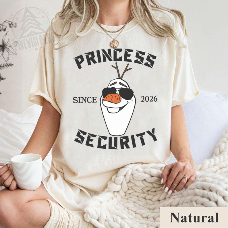 May include: Cream-colored t-shirt featuring a graphic of Olaf from Frozen wearing sunglasses and a carrot nose. The text reads "PRINCESS SECURITY SINCE 2026". The shirt is a relaxed fit.