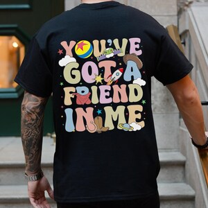 Puede incluir: Camiseta negra con un estampado gr&aacute;fico colorido que dice "You've Got a Friend in Me" con im&aacute;genes de dibujos animados de Woody, Buzz Lightyear y otros personajes de la franquicia de pel&iacute;culas Toy Story.