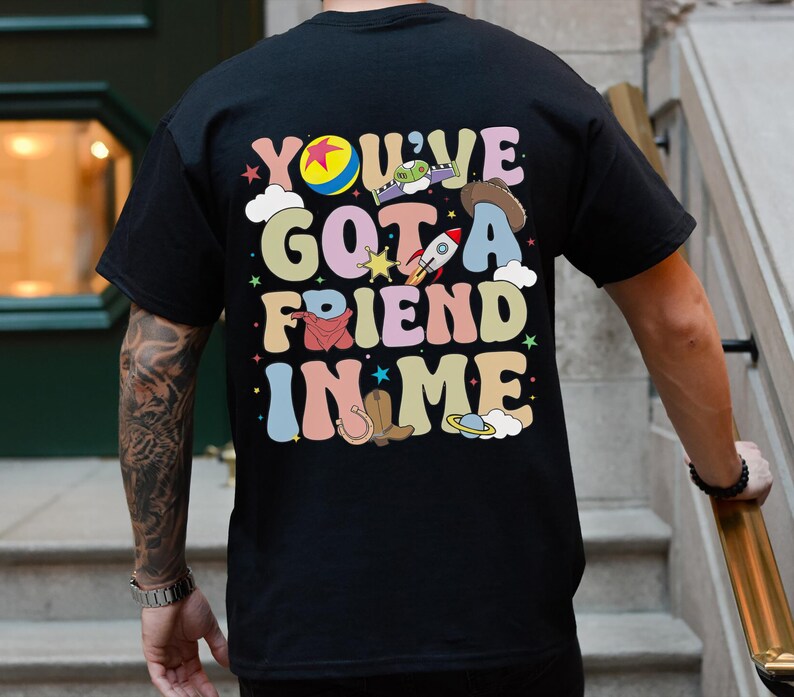Puede incluir: Camiseta negra con un estampado gr&aacute;fico colorido que dice "You've Got a Friend in Me" con im&aacute;genes de dibujos animados de Woody, Buzz Lightyear y otros personajes de la franquicia de pel&iacute;culas Toy Story.