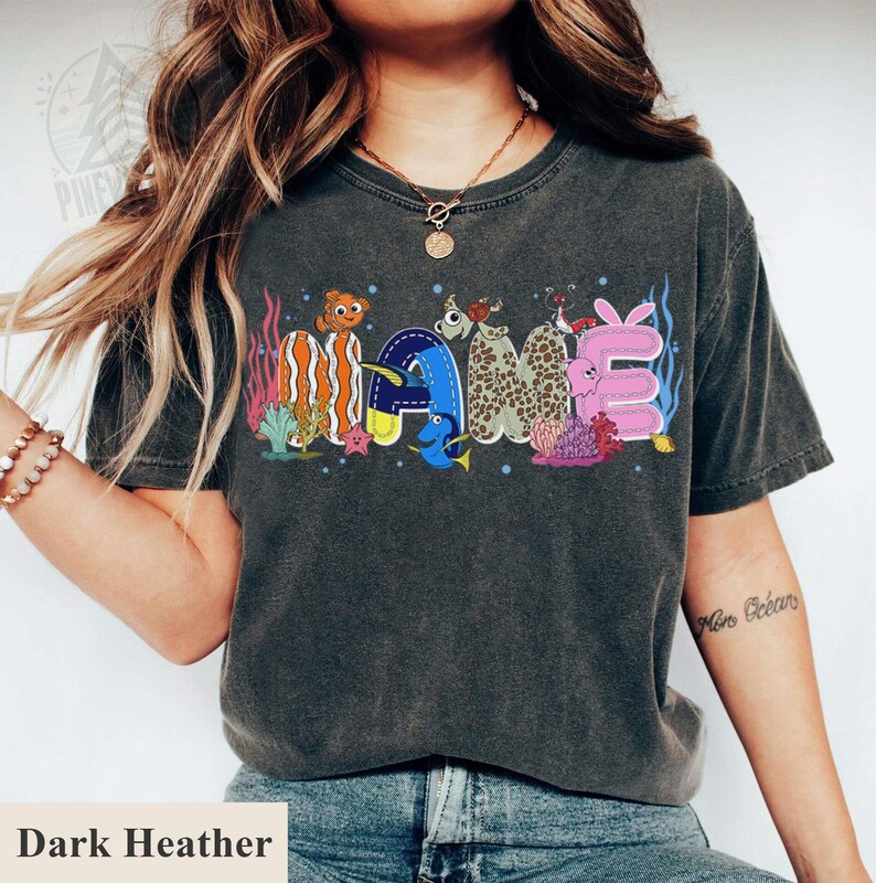 May include: Dark heather gray t-shirt with the word "NAME" in colorful, cartoonish, underwater-themed letters. The letters are decorated with sea creatures and coral. The shirt is a comfortable, casual style.