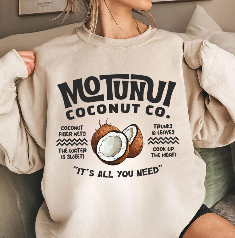May include: Beige sweatshirt with the text "MOTUNUI COCONUT CO." in black. The design includes illustrations of coconuts and text about coconut products. The phrase "IT'S ALL YOU NEED" is at the bottom.