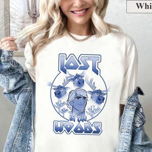 May include: White t-shirt with a blue graphic of a cartoon character with three reindeer. The graphic says "Lost in the Woods" in a stylized font.