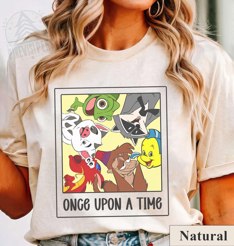 Op de afbeelding: Cr&egrave;mekleurig T-shirt met een ingelijste afbeelding van stripfiguren. De afbeelding bevat een kikker, een wasbeer, een varken, een vis en andere personages. De tekst "ONCE UPON A TIME" staat eronder. Het woord "Natural" staat rechtsonder.
