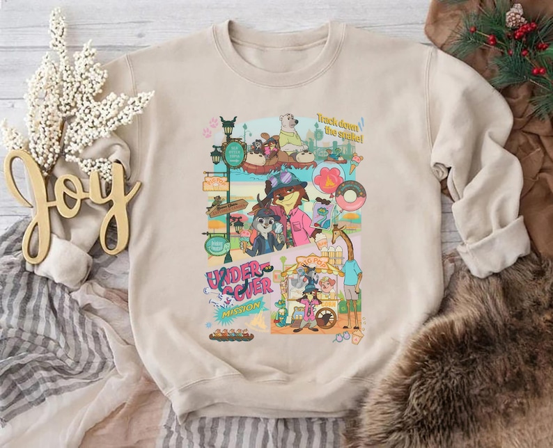 May include: Beige crewneck sweatshirt featuring a colorful cartoon graphic. The graphic includes various characters, signs, and the text "Undercover Mission" and "Track down the spike!"