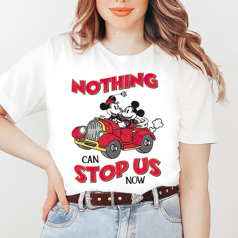 May include: White t-shirt with a red, yellow, and black cartoon image of Mickey Mouse and Minnie Mouse driving a red car. The text "NOTHING CAN STOP US NOW" is printed in red on the shirt.
